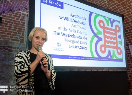 fotografia. projekcja filmu w ramach festiwalu art piknik w willi decjusza. Edyta Eliza Bojanowska z Centrum Czeskiego w Warszawie wygłasza wprowadzenie do filmu. w tle grafika promująca festiwal.